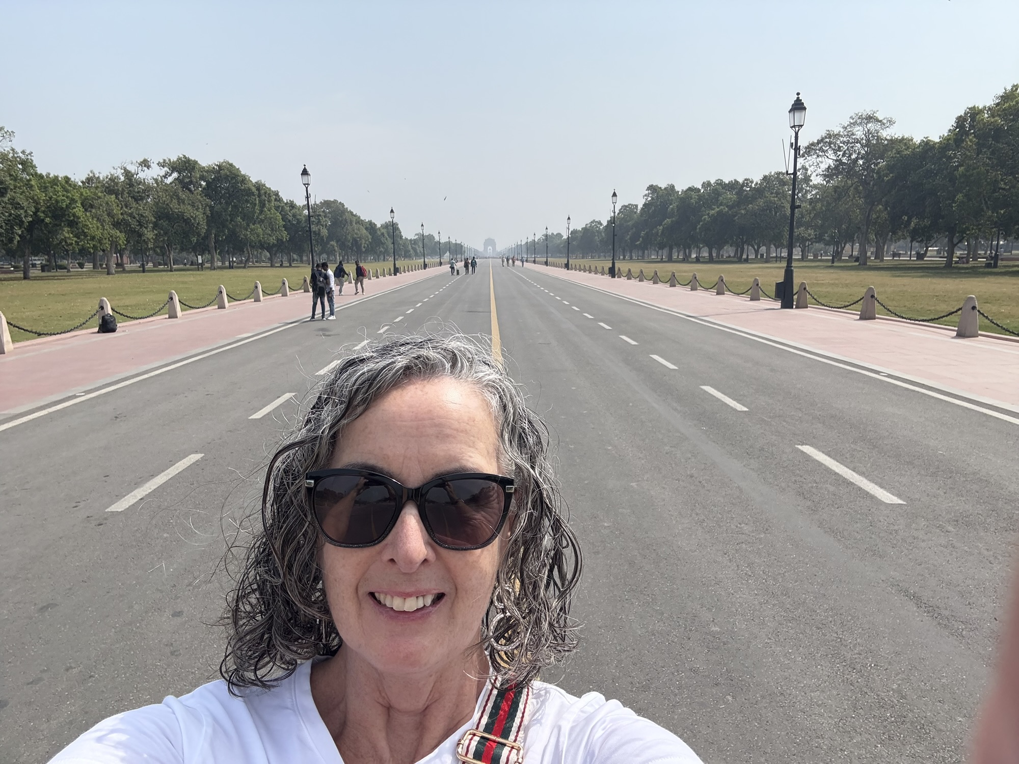 Mairead wearing sunglasses, takes a selfie on the Kartavya Path, in Delhi, with India Gate in the far background
