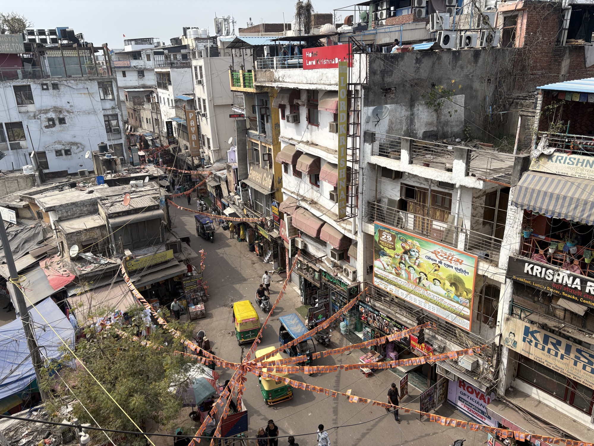 A view of Main Bazaar Road in Delhi, with tuk tuks and bicycles driving past, taken from a rooftop vantage point.