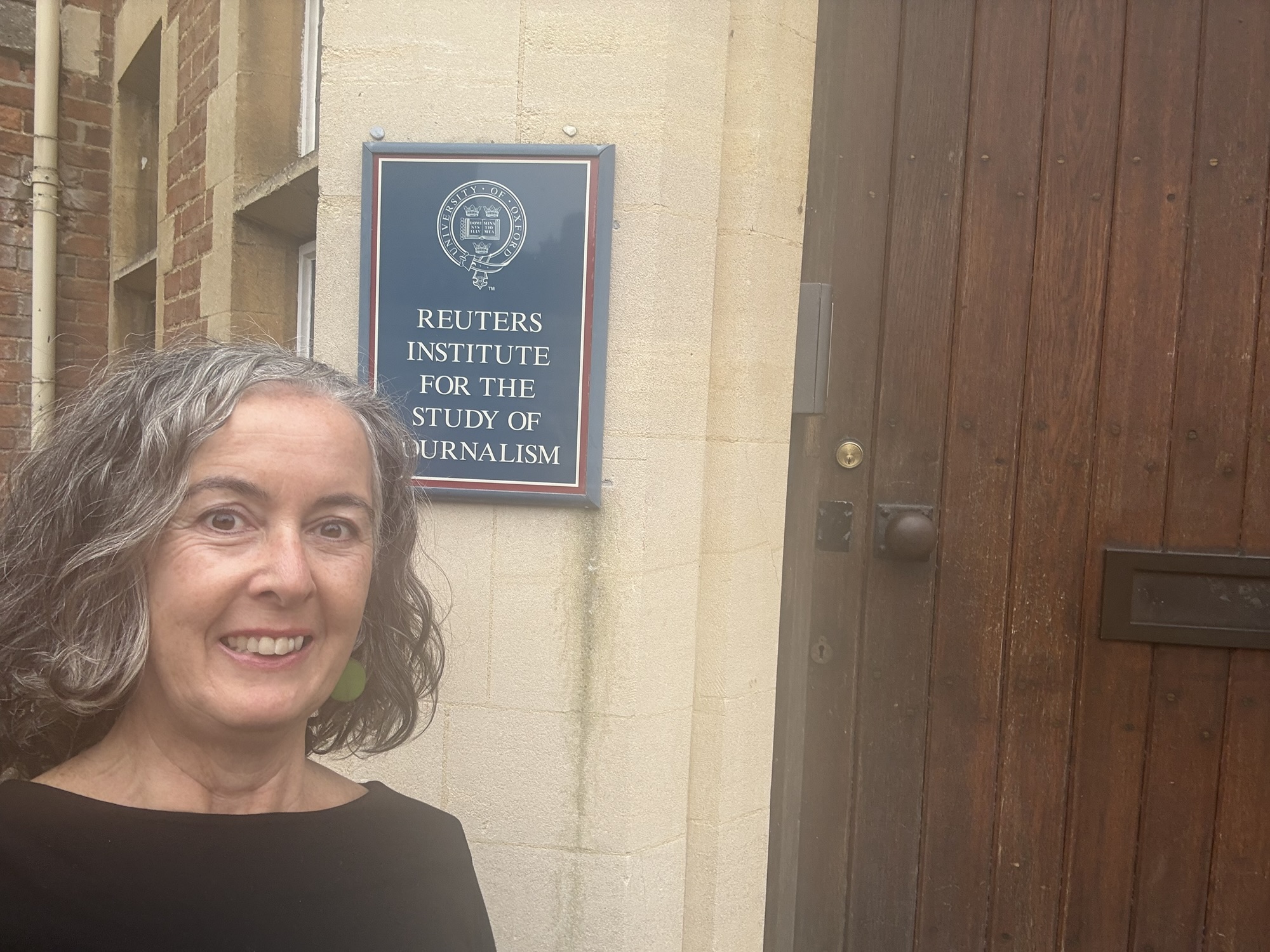 A person standing outside the Reuters Institute for the Study of Journalism, posing next to the institute's sign.